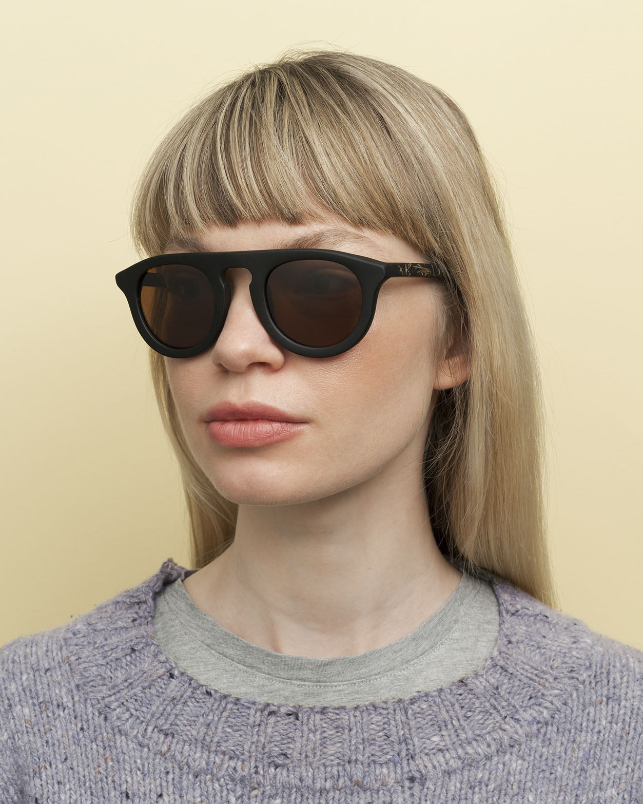 Laden Sie das Bild in den Galerie-Viewer, Woman wearing elegant sunglasses with warm brown lenses, emphasizing the contrast of flax temples and polished black frame.