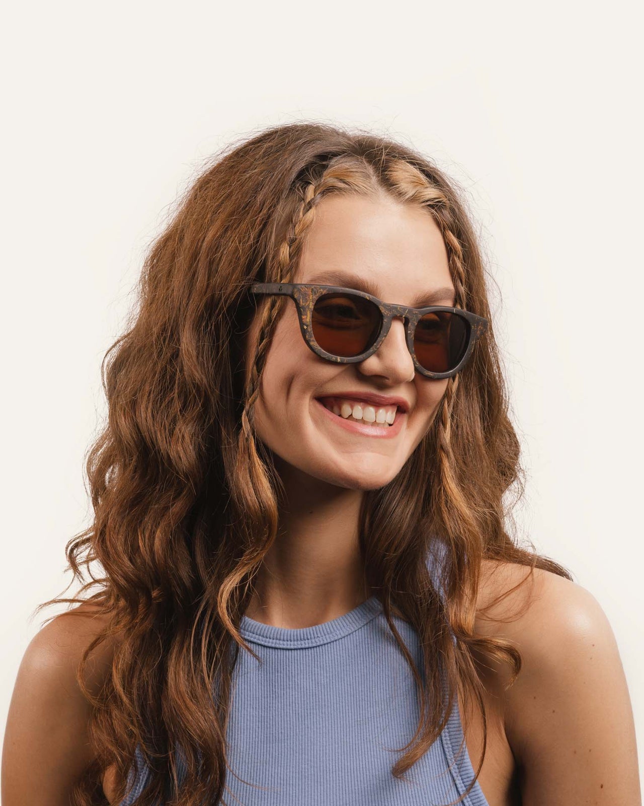 Laden Sie das Bild in den Galerie-Viewer, Woman smiling in eco-friendly sunglasses, highlighting their floral-inspired design and warm-toned lenses.