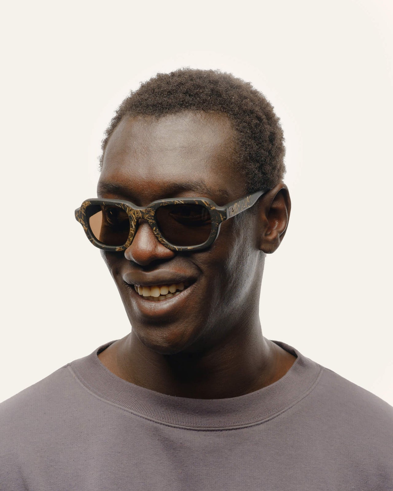 Laden Sie das Bild in den Galerie-Viewer, Smiling man wearing eco-friendly sunglasses with brown lenses and black frames.