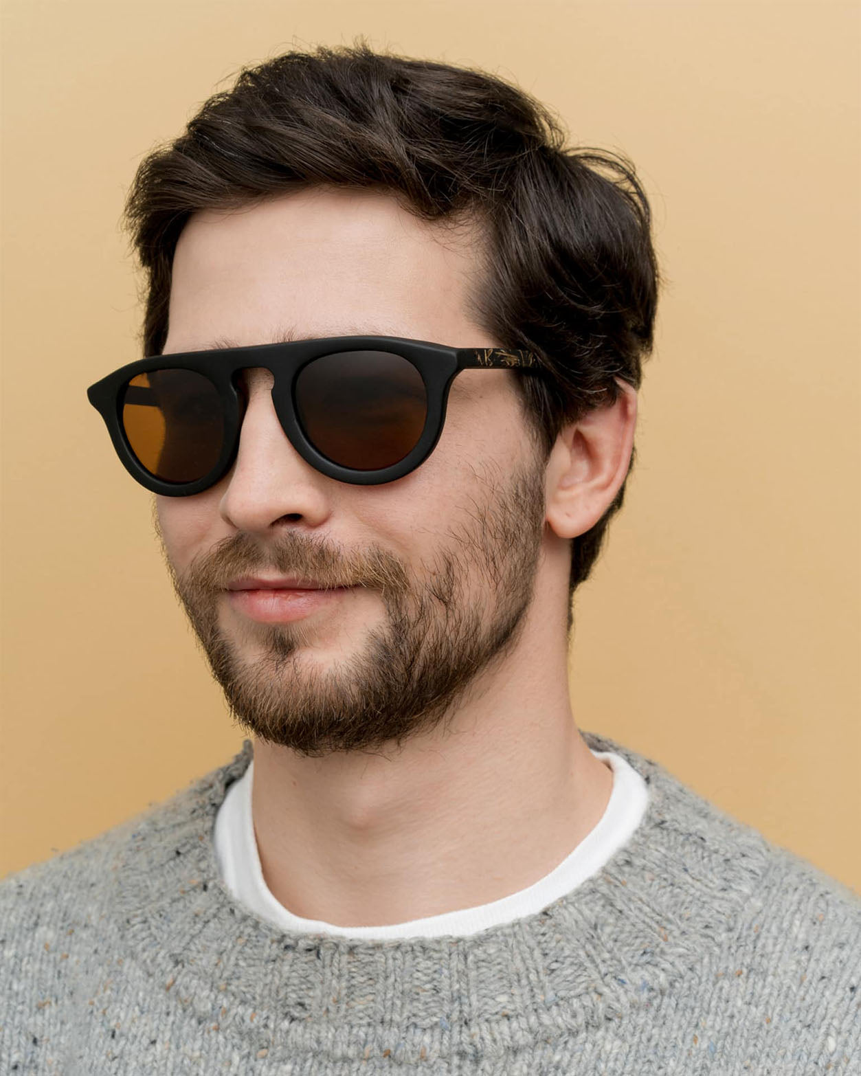 Man wearing eco-friendly sunglasses with brown lenses, featuring black coffee-based frames and flax-covered temples.