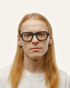 A man wearing black optical glasses with transparent lenses, showcasing their eco-friendly and sleek design.