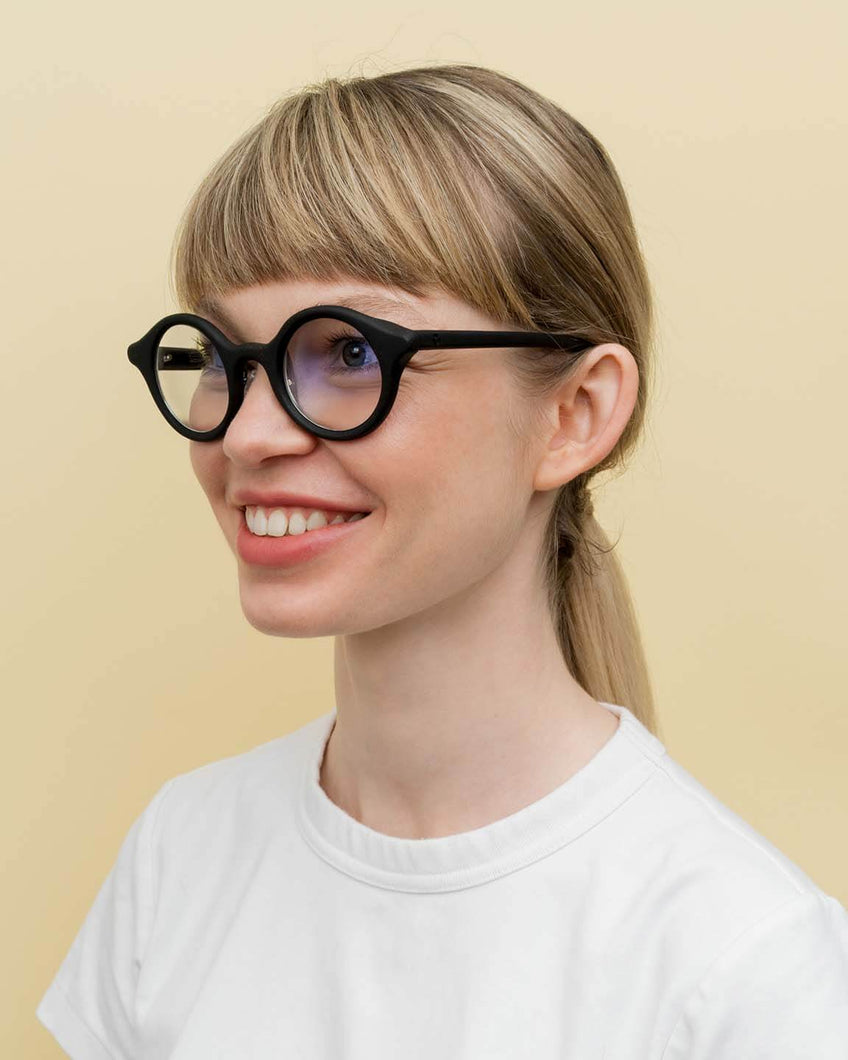 Smiling woman wearing black round coffee-based optical frames, perfect for sustainable everyday style.