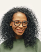 Woman with curly hair wearing sustainable optical frames, featuring coffee-based black material with flax detailing.