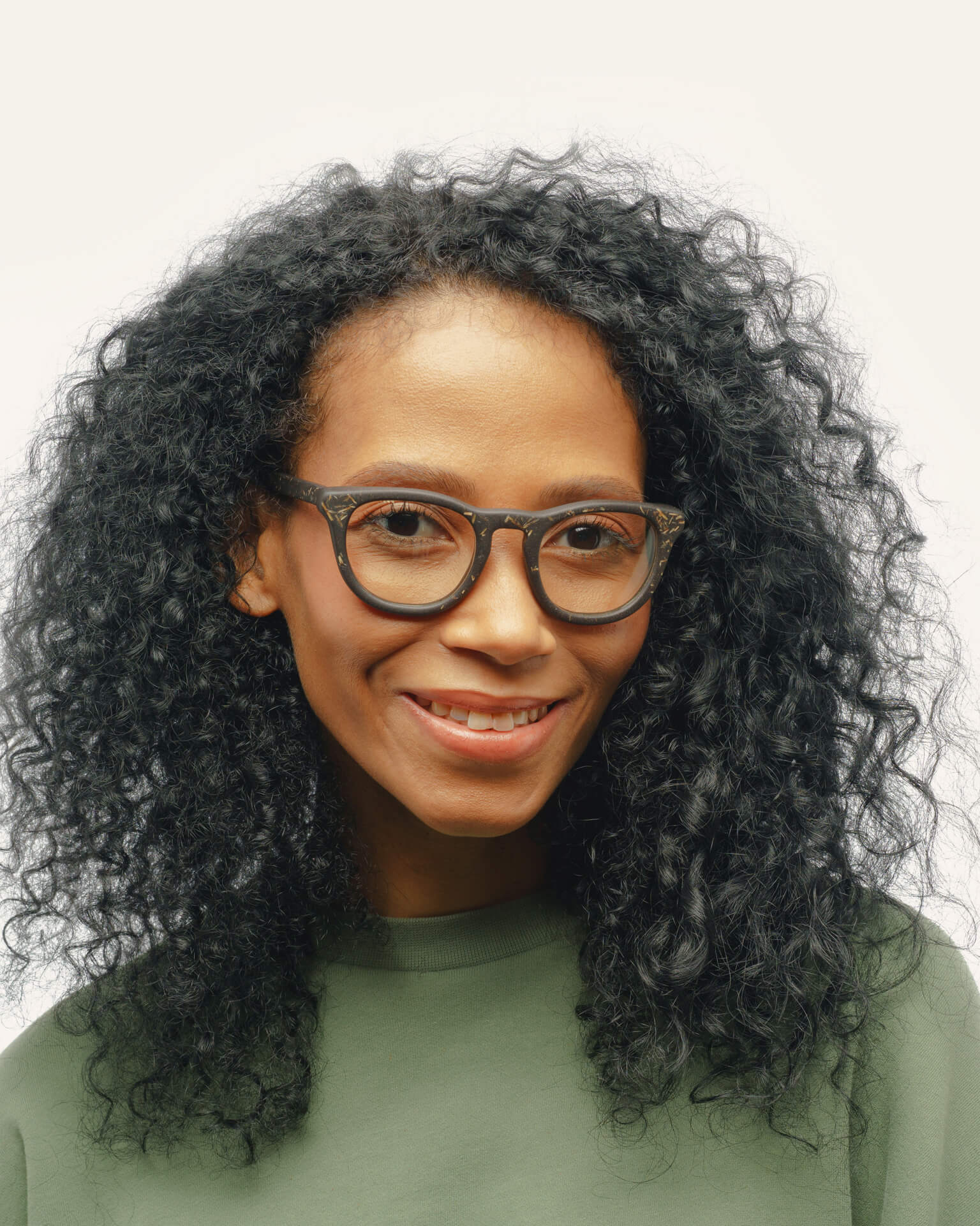 Woman with curly hair wearing sustainable optical frames, featuring coffee-based black material with flax detailing.