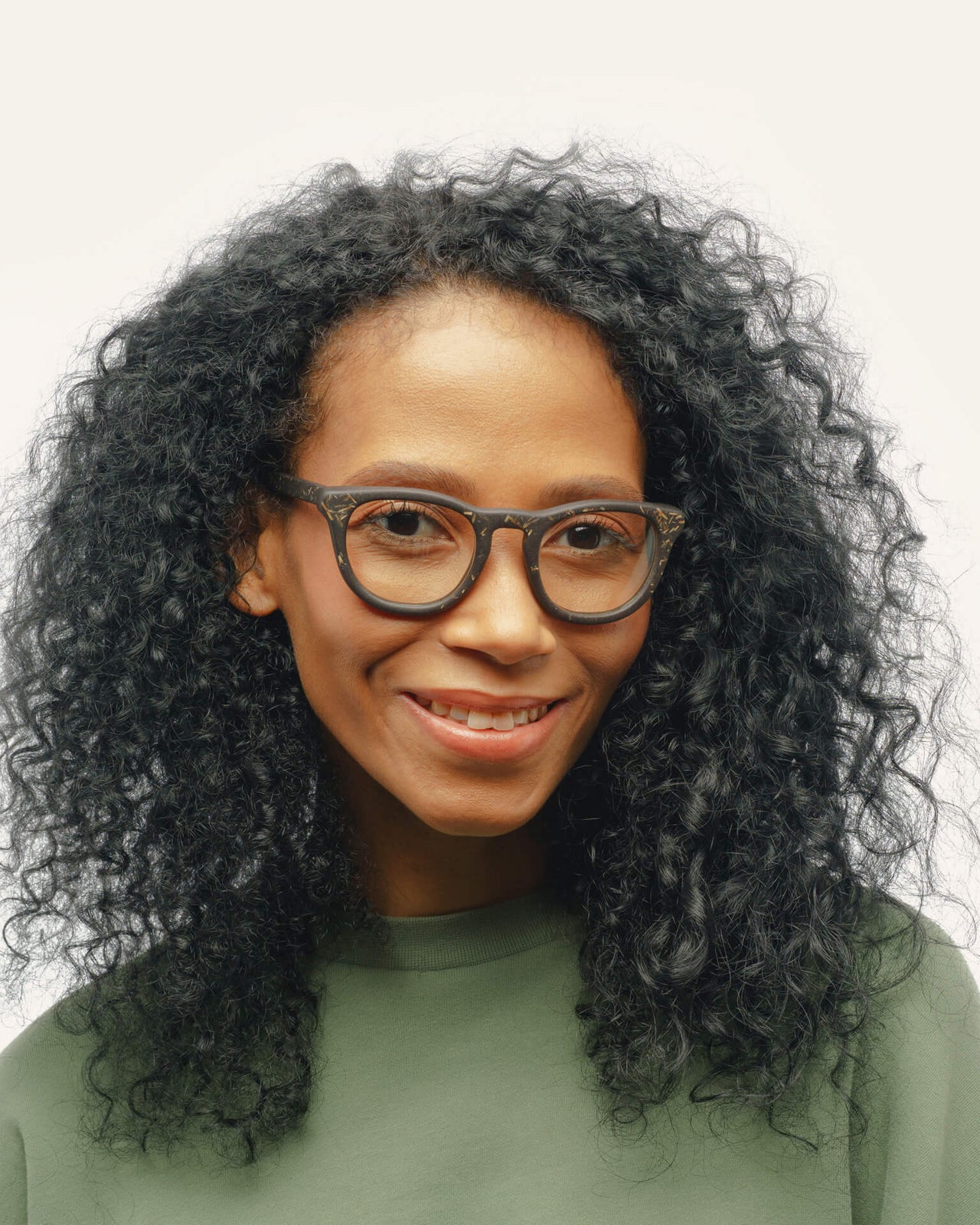 Laden Sie das Bild in den Galerie-Viewer, Woman with curly hair wearing sustainable optical frames, featuring coffee-based black material with flax detailing.
