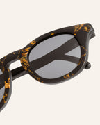Close-up of lightweight sunglasses, featuring artistic sunflower petal textures on a coffee-based frame.