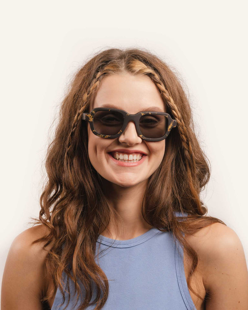 Sunglasses with gray lenses and a sunflower-accented coffee-based frame displayed on a neutral background