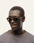 Smiling man wearing eco-friendly sunglasses with brown lenses and black frames.
