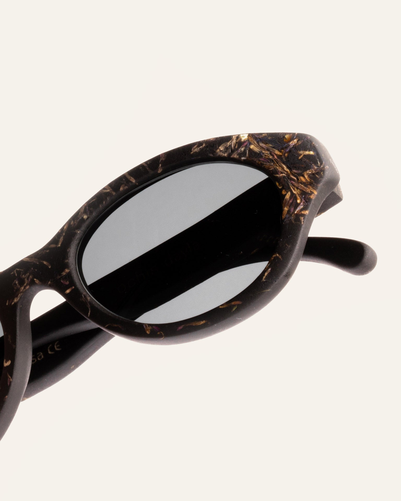 Close-up of natural coffee-based sunglasses, highlighting delicate cornflower petal details and sleek gray lenses