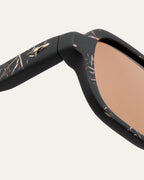 Close-up of textured black frame with natural flax accents and warm brown lenses.