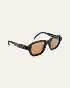 Angled view of black sunglasses with flax details and brown lenses.