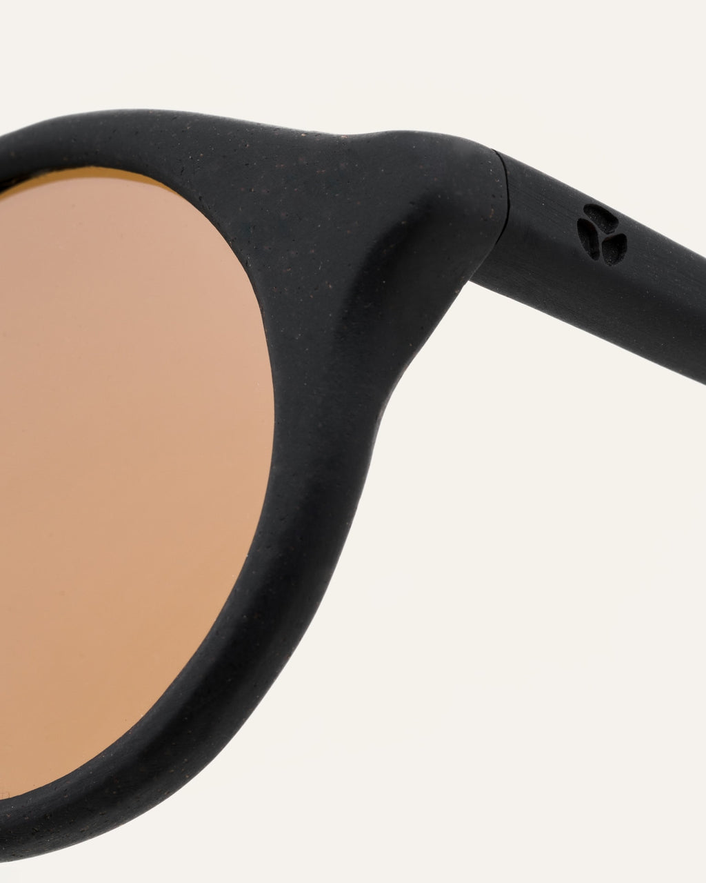 Close-up of brown lenses in round black sunglasses, highlighting the polished coffee-based frame and handcrafted quality.