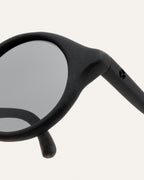 Close-up of gray lenses in round black sunglasses, showing the smooth frame finish and attention to detail.